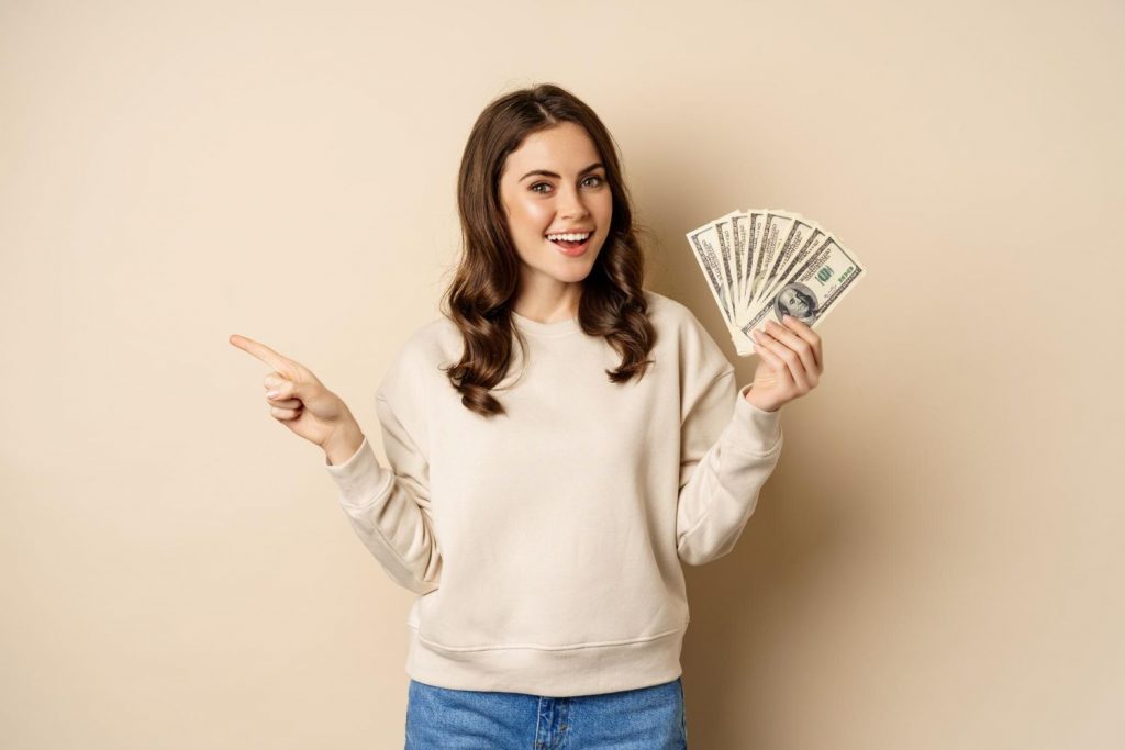 A happy woman holding dollar bills and pointing sideways — representing Affiliate Marketing success and earning money through the right affiliate programs.